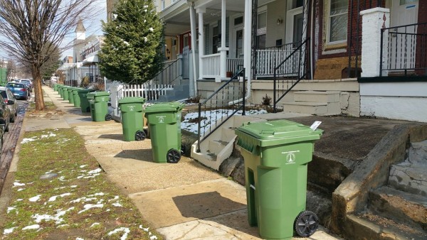 several green trash cans lined up on the sidewalk