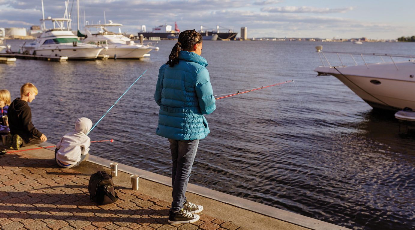 A girl casts off at a pier in Baltimore's Inner Harbor. This image is featured in Blue Water Baltimore's 2018 annual report.