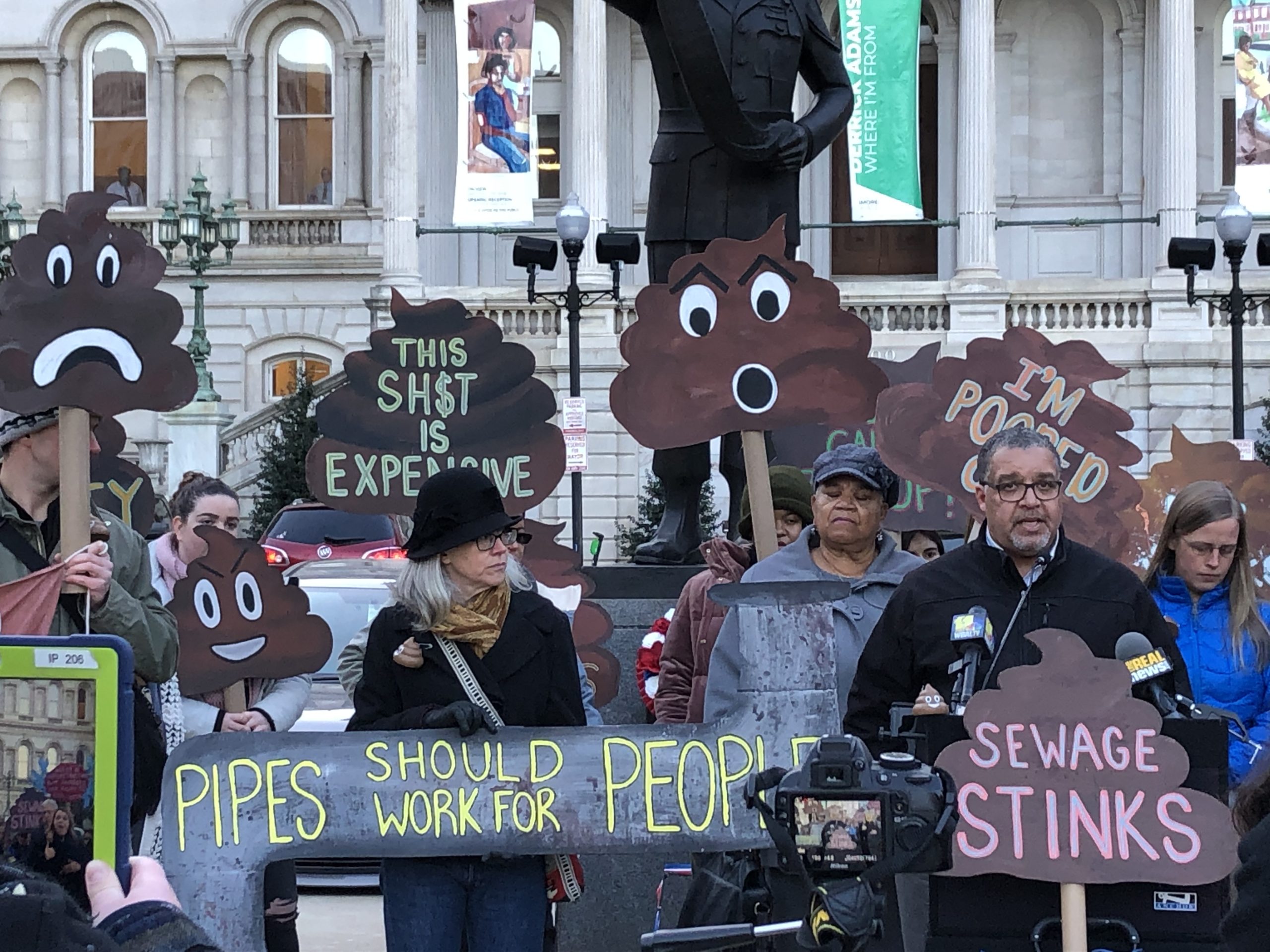Community members rally in front of City Hall in November 2019 with poop-shaped signs with slogans like "sewage stinks!"