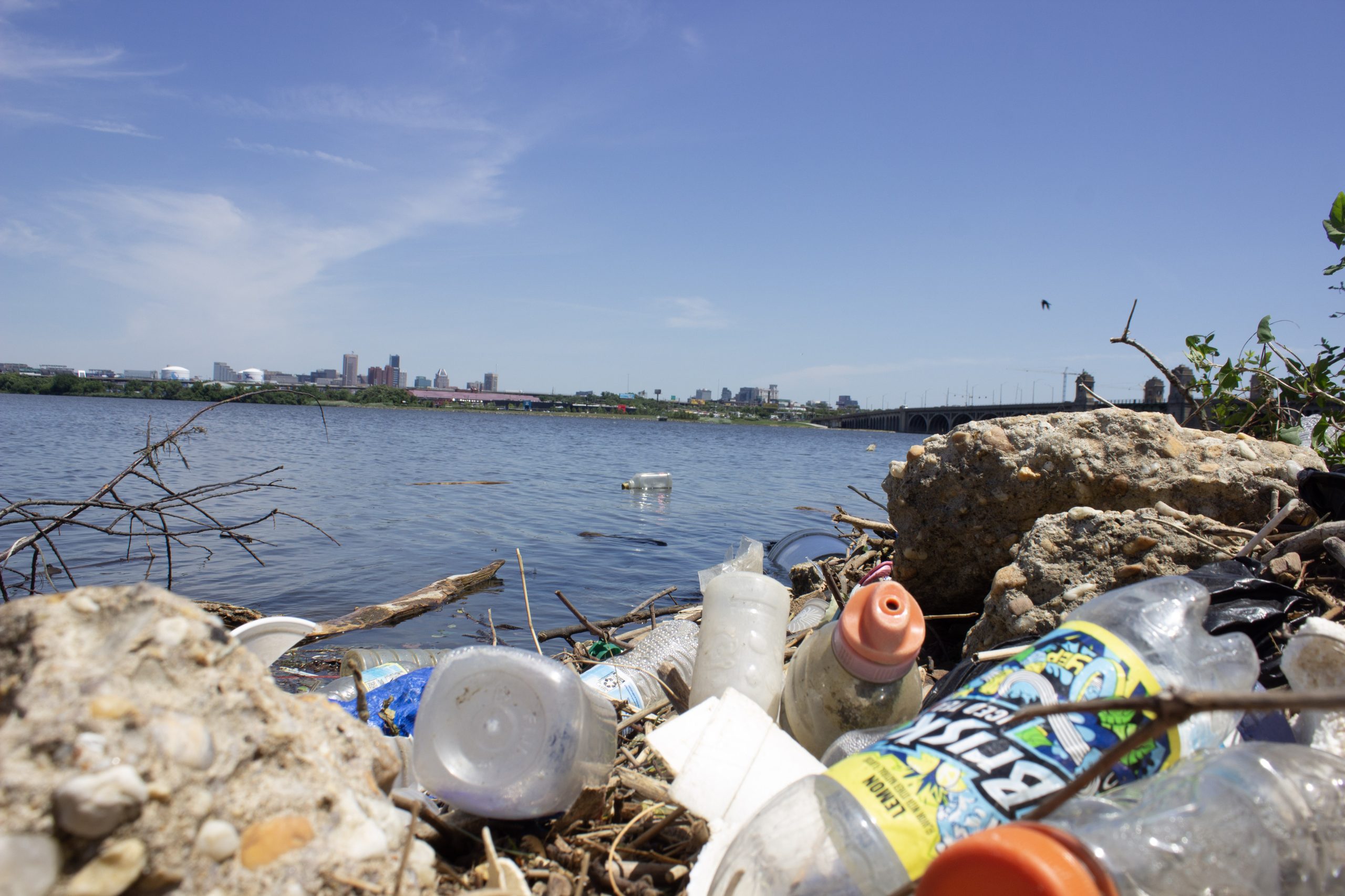 Picture of trash, mainly bottles, on the bank of a waterway.