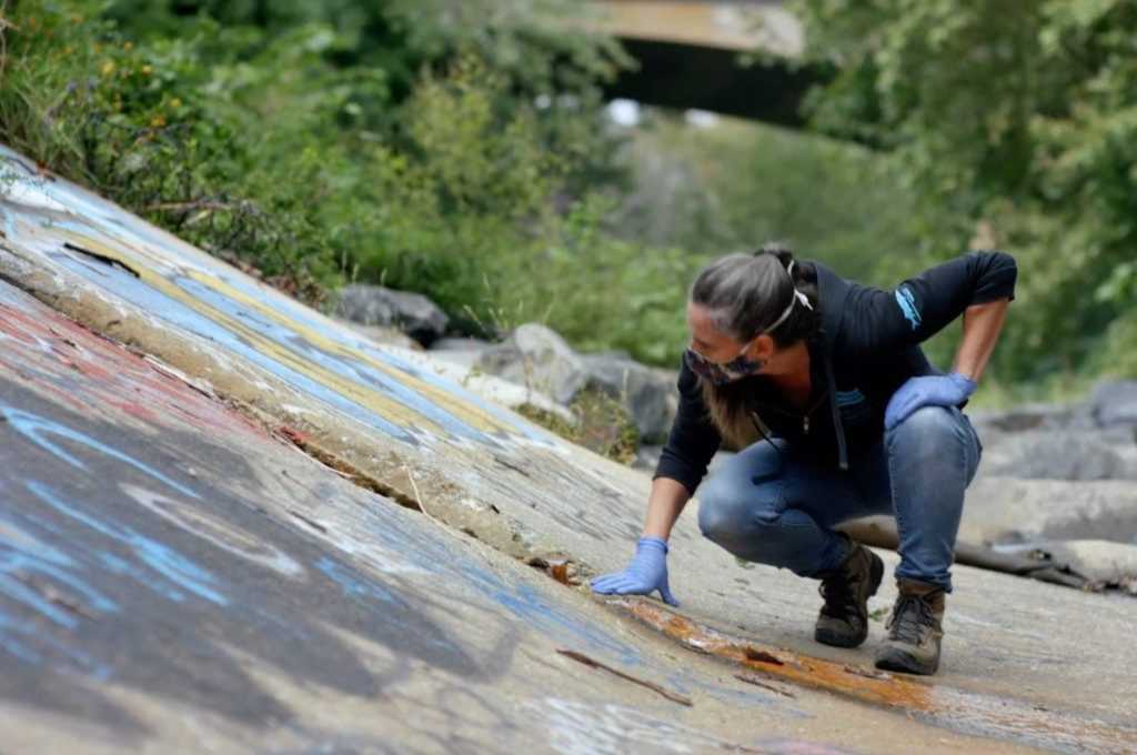 a woman crouches down to paint on a rock