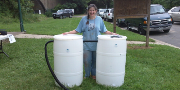 A woman pictured next to two white rain barrels.
