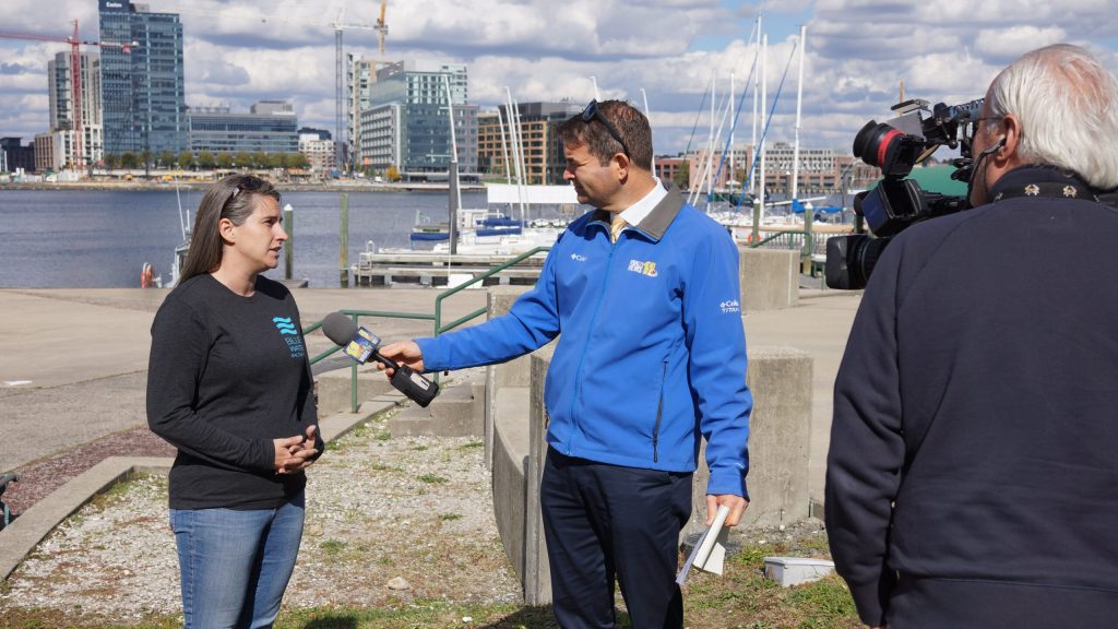 Baltimore Harbor Waterkeeper is interviewed by TV news crew, harbor is visible in the background.