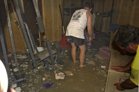 Backed up sewers can cause thousands of dollars in damage to floors, furniture, and priceless items such as family photos (Credit: Marvin Nauman / FEMA). Alt text: Two men removing belongings without protective equipment from a basement during a sewage backup.