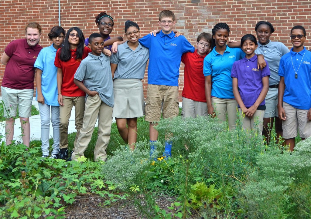 Students from Sudbrook smile as they gather in front of the garden, blooming with native plants that they installed.