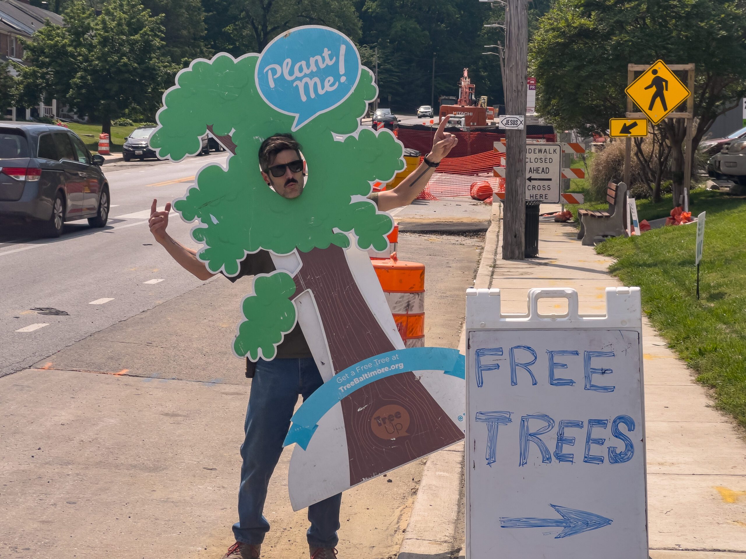 a man holding up a tree sign on the side of a road