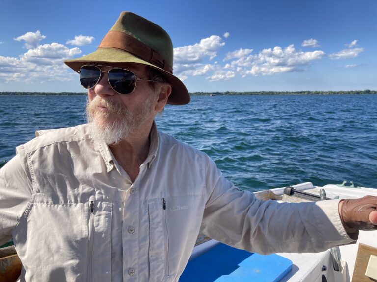Jack Boyson, wearing sunglasses and a hat steering a boat