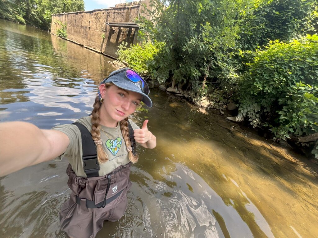 a woman standing in a river giving a thumbs up