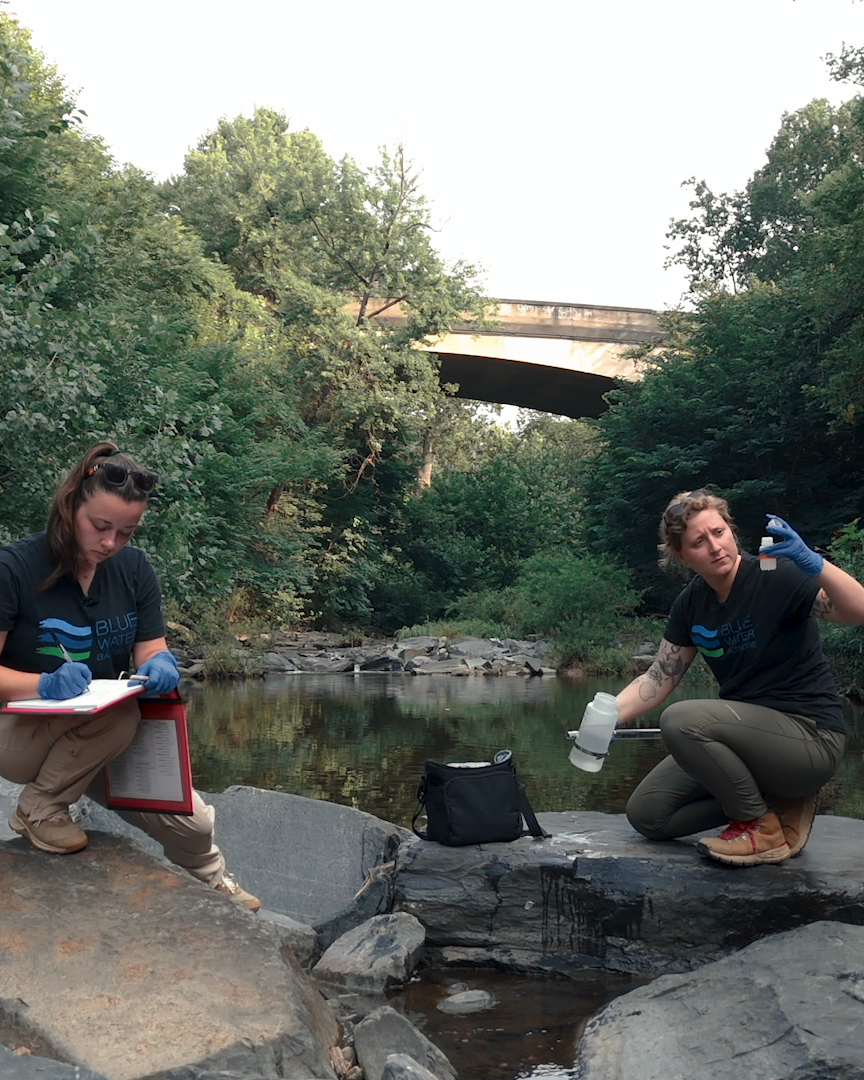 two people sitting on rocks near a river